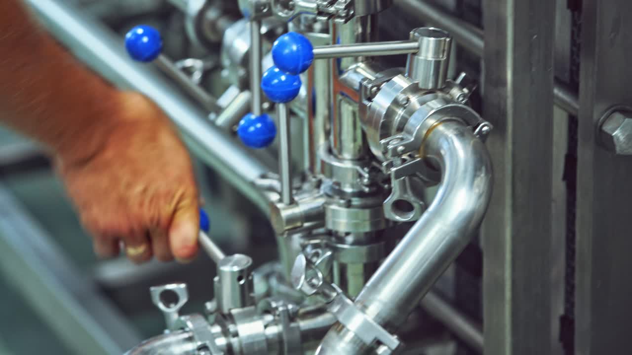 Worker switches on automated machine in a modern plant. Worker turning on metal tool to start the work of a modernized machine in a dairy factory. Close-up.
