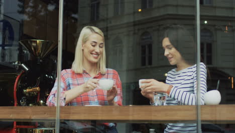 dos amigos sonrientes sentados en un café detrás de una ventana, tomando y bebiendo café