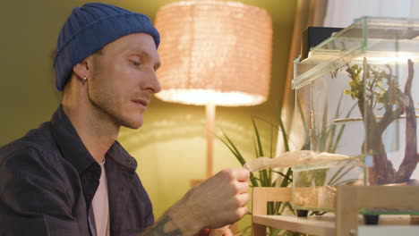 side view of a man picking up the shed skin of his snake from a terrarium