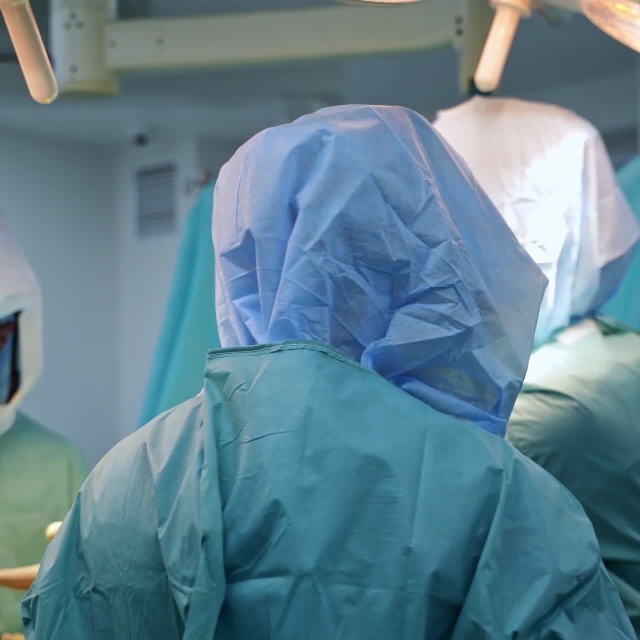 Team of doctors in protective suits in the operational room. Surgeon covering hands with antiseptic liquid