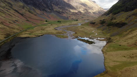 toma aérea sobre un pequeño lago y revelando las hermosas montañas ubicadas en el valle de las tierras altas de glencoe