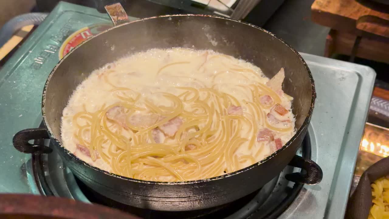 Spaghetti carbonara with bacon simmers in creamy sauce, overhead view, warm indoor lighting, minimal movement