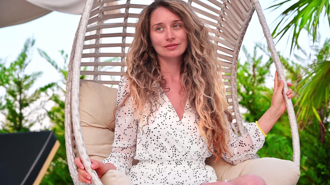A woman smiling and enjoying her vacation, resting in an armchair, swinging