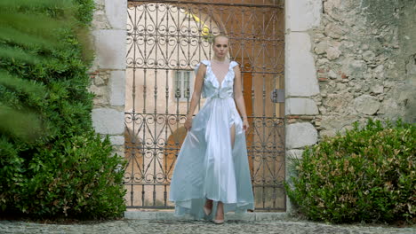 woman in a light blue satin dress at a stone gate