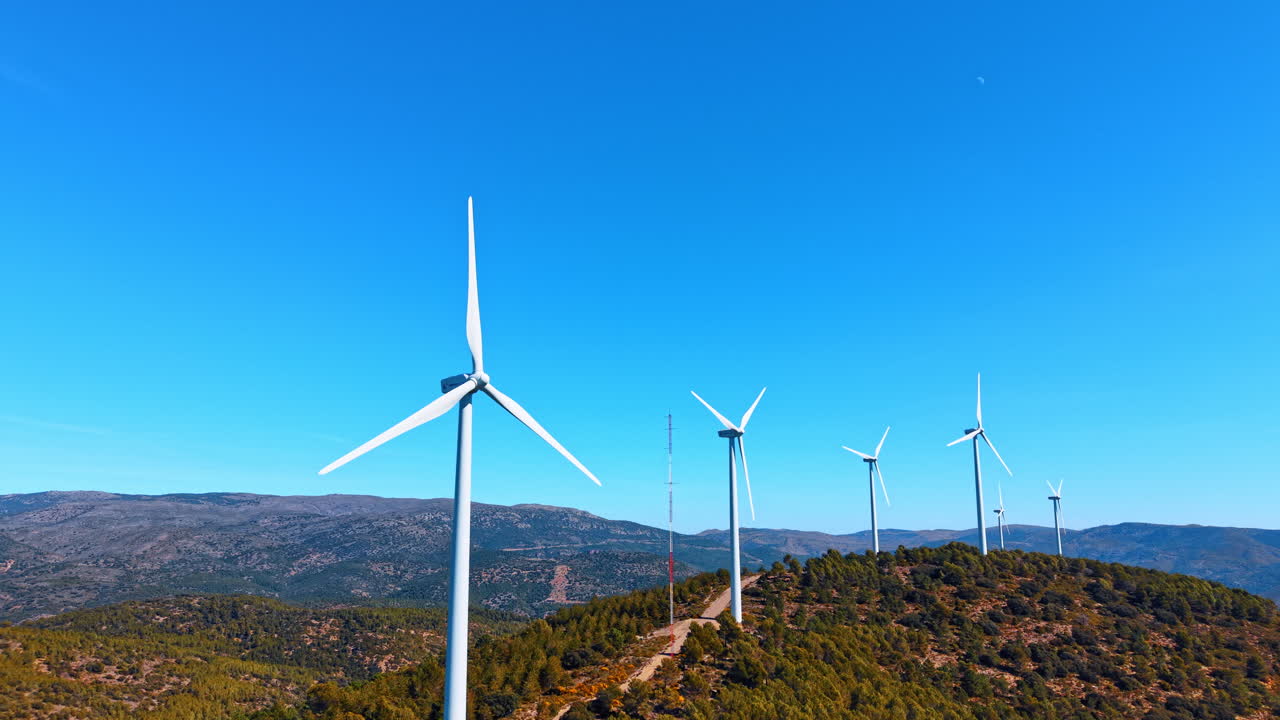 Alicante, Spagna, 8 agosto 2025: Fila di pale eoliche bianche contro un cielo azzurro limpido. Vista prospettica di generatori di energia eolica su una cresta di montagna nella Spagna rurale