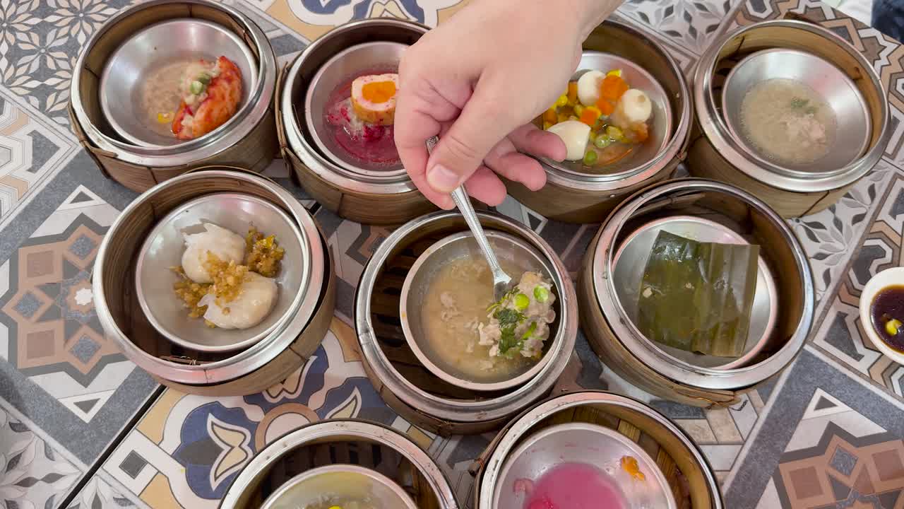 Hand serving shrimp dim sum from steamer baskets on patterned table under natural lighting