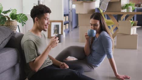 Feliz-Pareja-Birracial-Mudándose-De-Casa,-Sosteniendo-La-Llave-Y-Tomando-Café