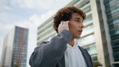 focused teenager talking earphones street portrait. curly guy touching earbuds