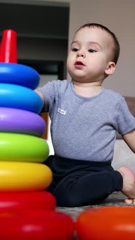 lovely kid takes the rings of pyramid from the floor. toddler constructs pyramid and learns size and colors. low angle view. vertical video