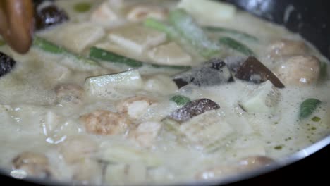 adding table spoon of salt sugar from small blue bowl to boiling thai vegetable curry