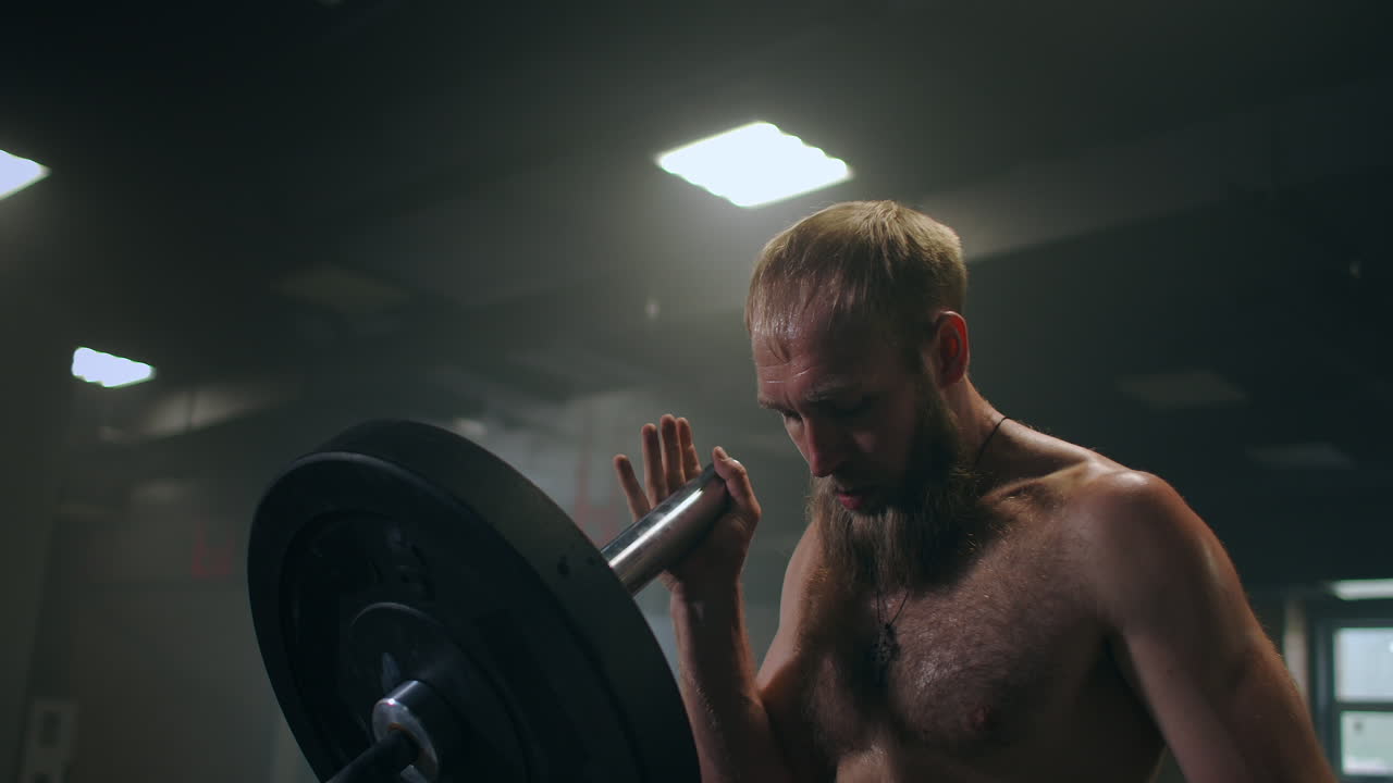 мальчик толкает штангу в тренажерном зале одной рукой. спортсмен без футболки в темной комнате поднимает штанга во время практики силы удара