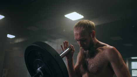 el niño empuja la barra en el gimnasio con una mano. un atleta sin camiseta en una habitación oscura levanta la barra mientras practica la fuerza del impacto