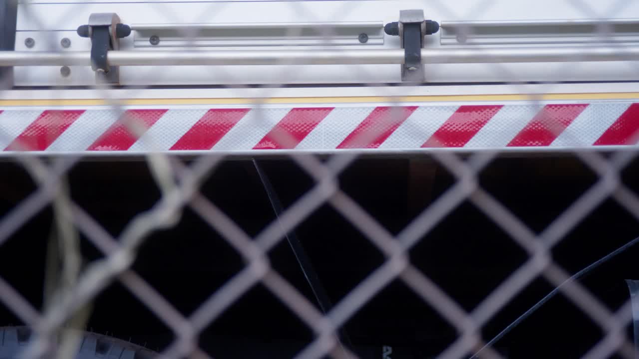 Lateral de un camión de bomberos rural detrás de una valla de tela metálica asegurada. Clip con movimiento de izquierda a derecha, enfocado en la franja de peligro lateral