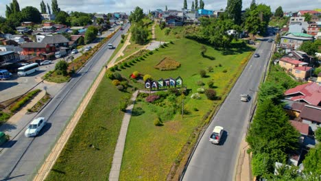 Drones-Aéreos-Vuelan-Sobre-Las-Carreteras-De-Entrada-De-La-Ciudad-En-América-Del-Sur-Ciudad-De-Castro-Chile-Parque-Urbano-Verde-Alrededor-De-Los-Autos-Conduciendo,-Casas-Tradicionales-Patagónicas,-Estableciendo-Un-Tiro