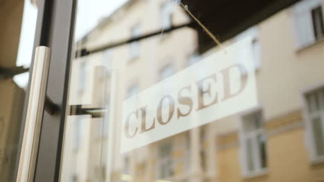 Close-up-view-of-young-man-hands-turning-over-a-signboard-closed"-on-the-door-of-coffee-shop"