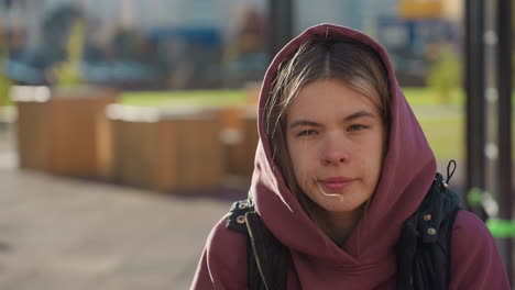 hoodie wearing athlete steadies self in forward pistol squat with hands on thigh as breeze lifts hair over urban garden path lined with flowering shrubs under warm sunlight and long soft shadows