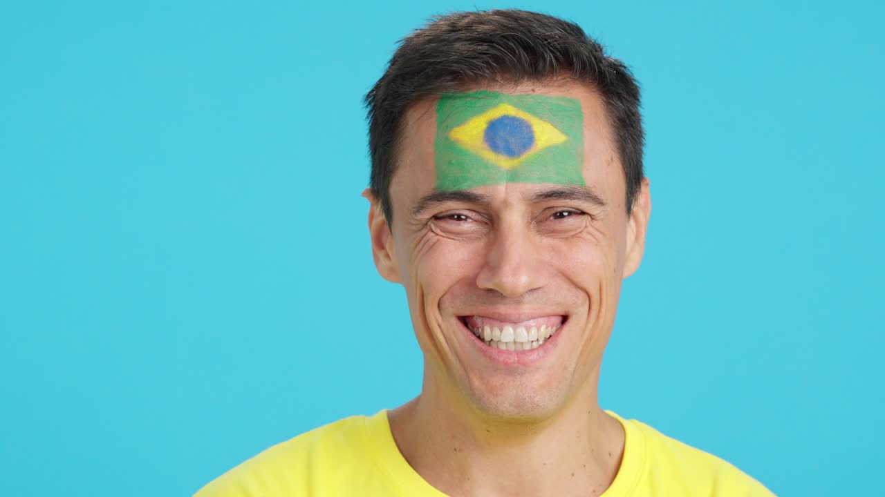 Hombre con una bandera brasileña pintada en la cara sonriendo