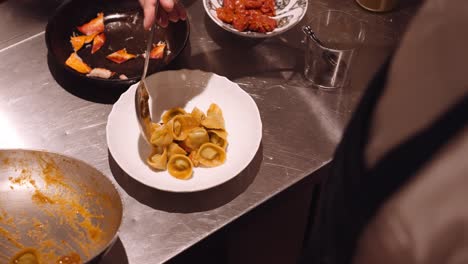 Cook-in-the-kitchen-of-an-Italian-restaurant-puts-the-ready-pasta-on-a-round-white-plate-with-extreme-precision