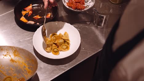 cook in the kitchen of an italian restaurant puts the ready pasta on a round white plate with extreme precision