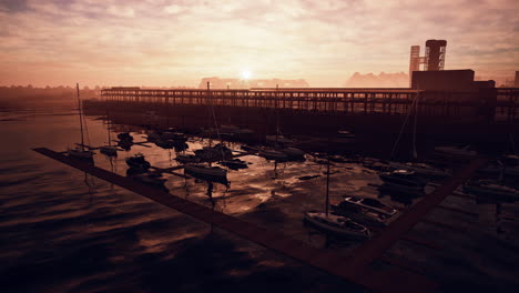 puesta de sol en un puerto deportivo con edificios industriales en el fondo