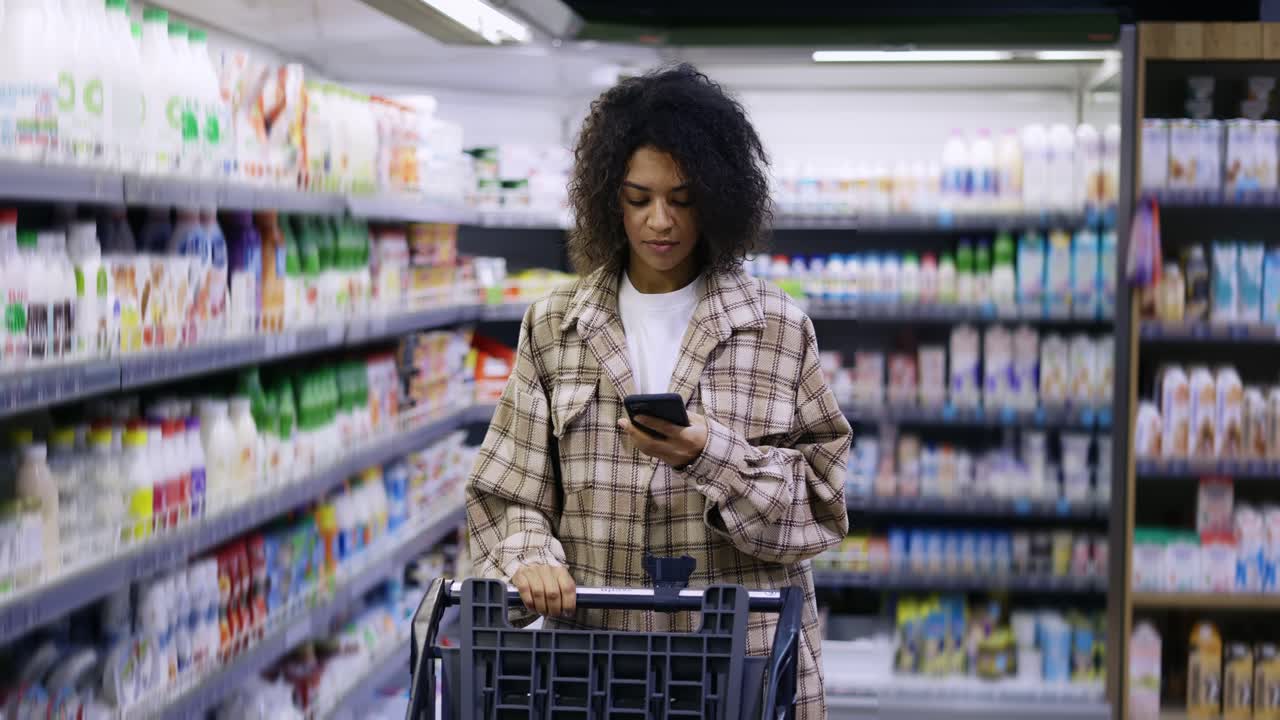 African American with shopping cart using smartphone at supermarket