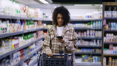 african american with shopping cart using smartphone at supermarket