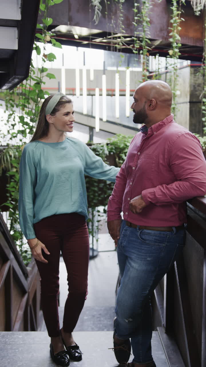 Vertical video of two happy diverse creative designers in discussion in casual office, slow motion