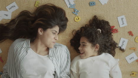 cheerful mother and daughter lying on the floor and chatting