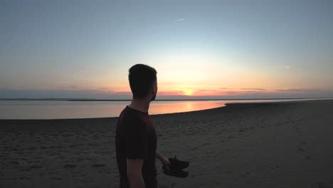 Hombre-Caminando-En-La-Playa-Con-La-Puesta-De-Sol-Y-El-Océano-Frente-A-él-En-Cámara-Lenta-De-Cerca