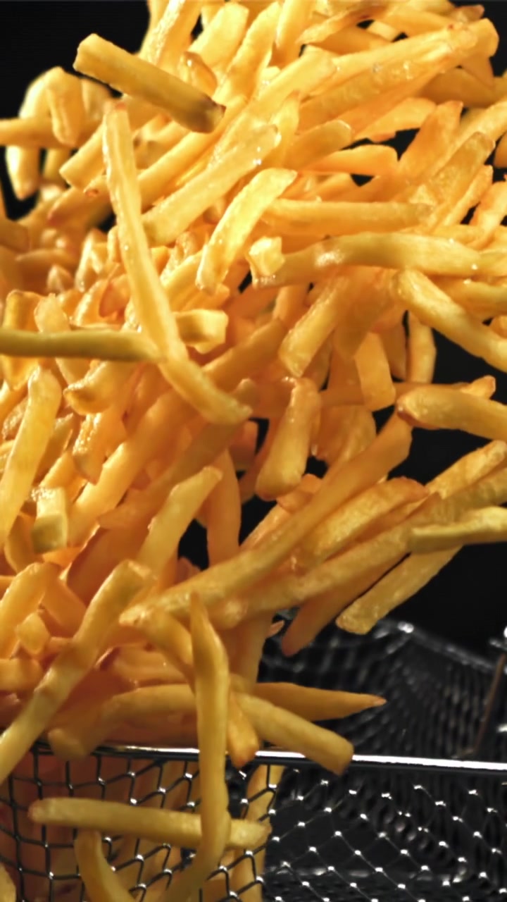 Gyllene pommes frites som faller från en fritöskorg i slow motion
