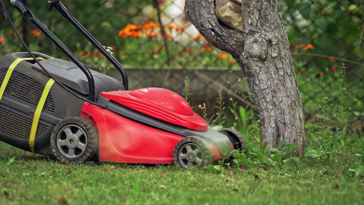 Gartenarbeit im Hintergrund. Gärtner mäht das Gras mit rotem Elektromäher.