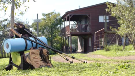 Hiking-shoes,-sticks,-mat-and-backpack-lying-on-grass-at-log-cabin,-slow-motion