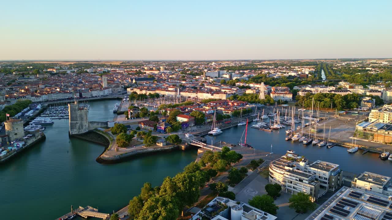 Drone shot at sunset showing the harbor of La Rochelle with its towers, docks, boats, waterfront buildings and the city stretching into the distance. - France