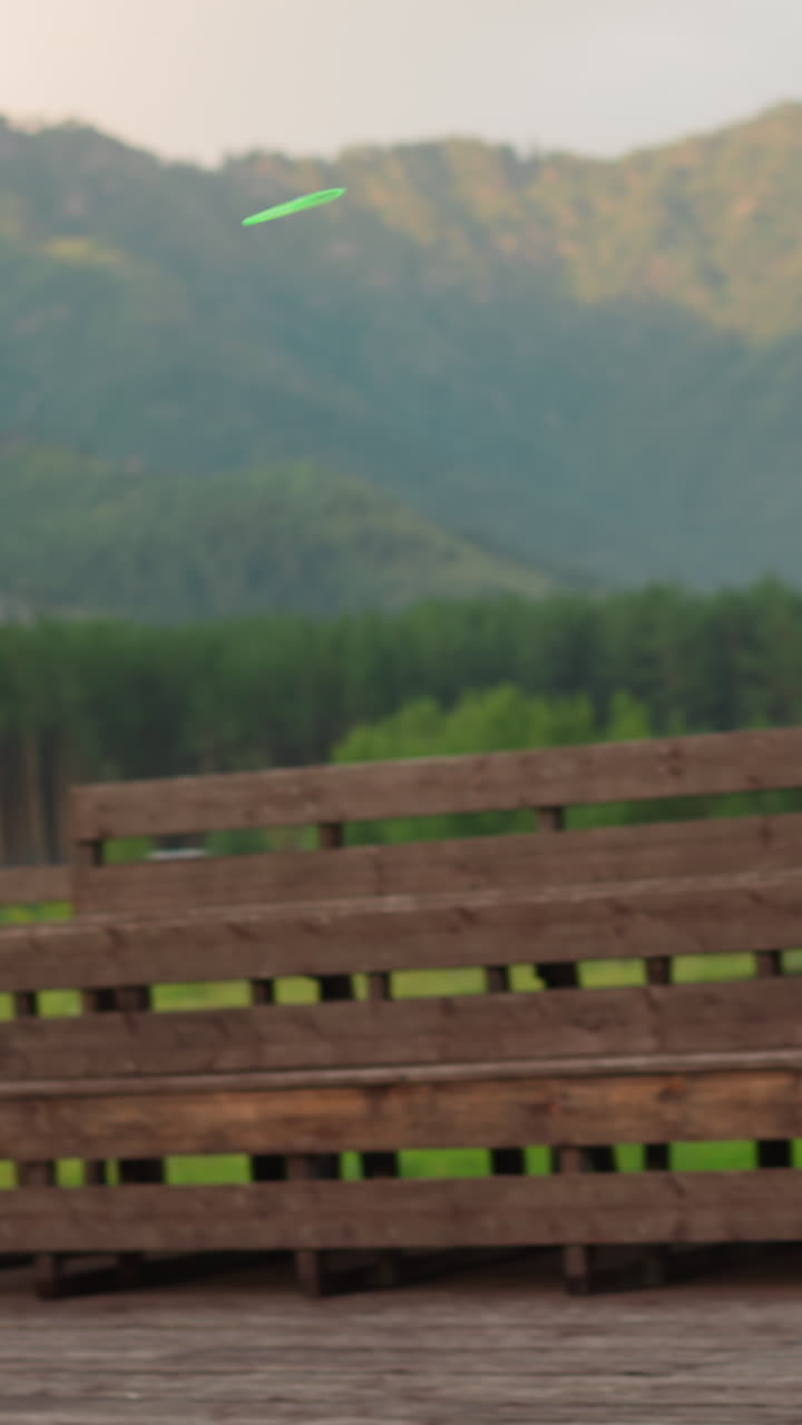 Little boy launches flying toy standing on dance ground with benches at highland eco resort against large mountains in spring slow motion
