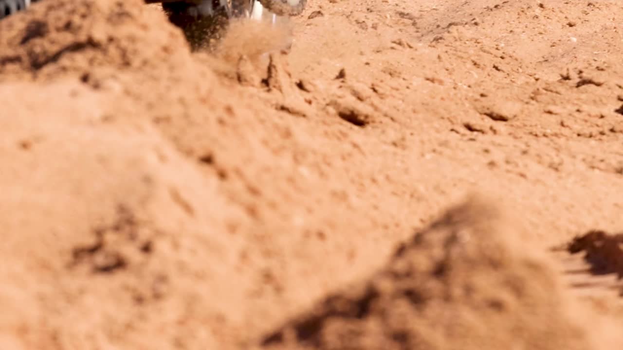 A detailed view of dirt bike tires navigating a sandy trail, showcasing tire tracks and sandy terrain.