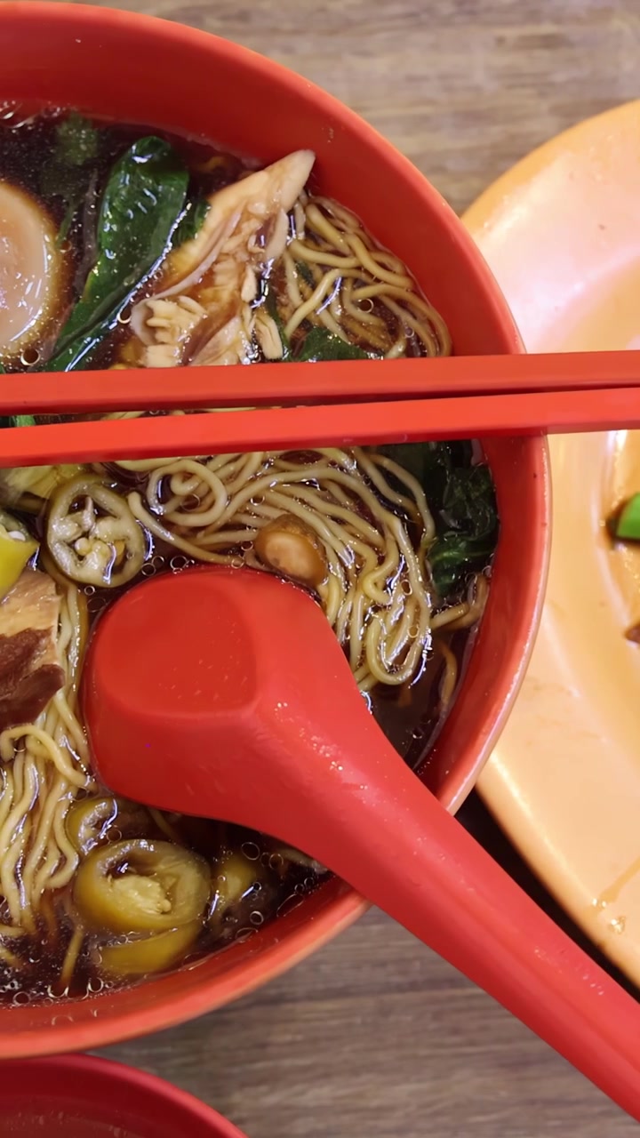 La telecamera si sposta da un piatto di broccoli cinesi con salsa a una vivace ciotola di zuppa di noodle arrostiti, mettendo in risalto ingredienti freschi sotto un'illuminazione brillante e uniforme.