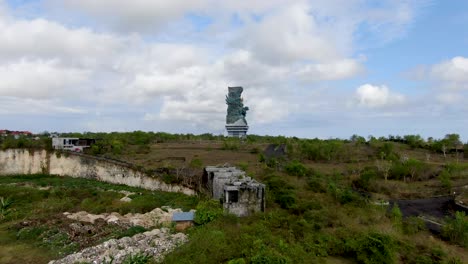 Huge-ancient-statue-in-middle-of-vibrant-green-Bali-landscape,-aerial-view