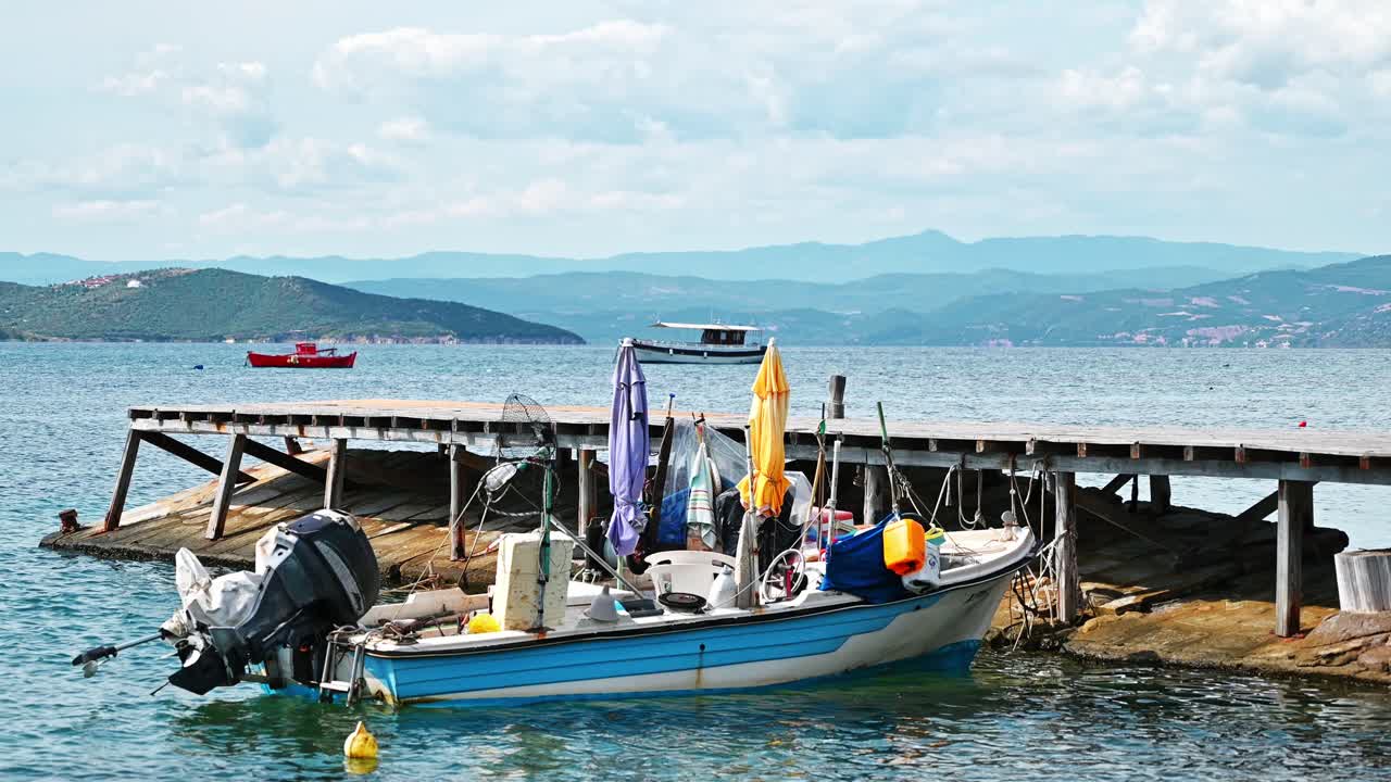 Beached metal motorized colored boat on a pier on Aegean sea coast, hills and a town on the background in Ouranoupolis, Greece