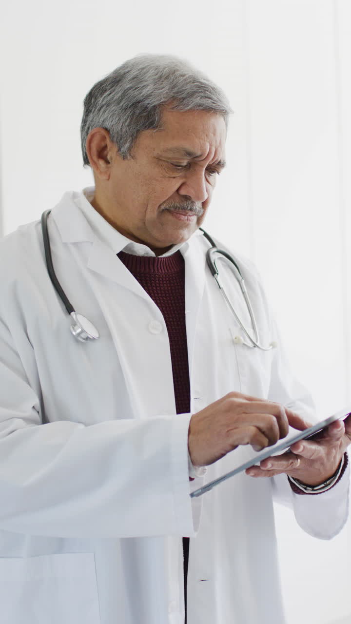 Vertical video of senior biracial male doctor using tablet