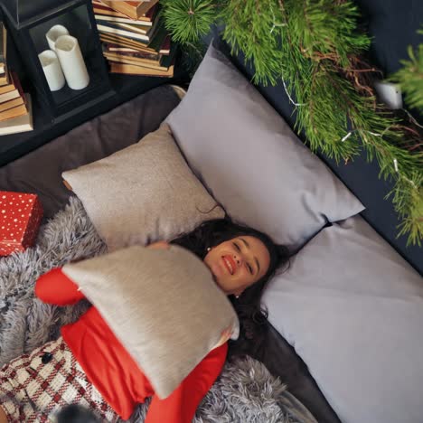 cute woman throws pillow to the air laying on bed. room decorated before christmas. video from the top