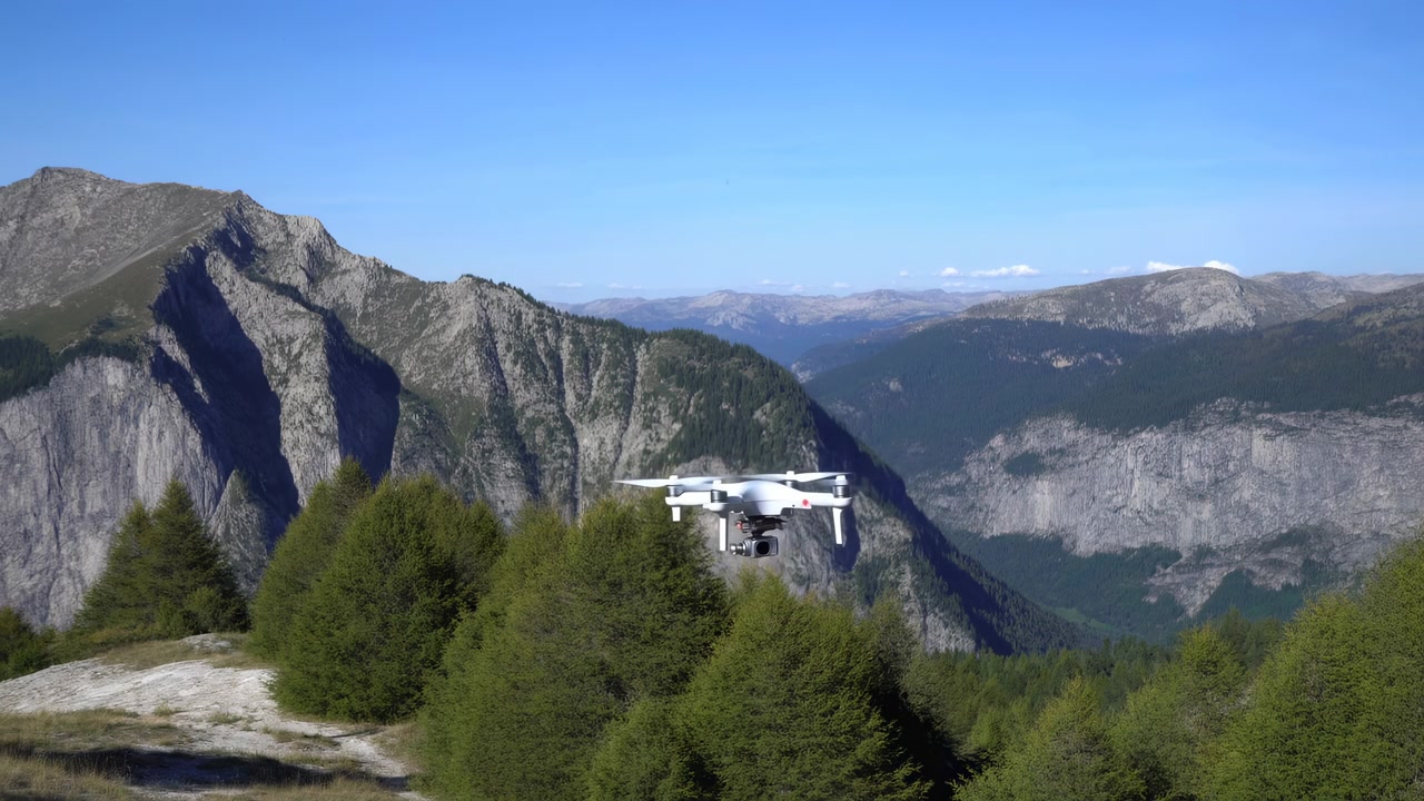 Un piccolo quadricottero bianco si muove attraverso un paesaggio montano scenografico, librandosi sopra fitte cime di alberi sempreverdi mentre scogliere rocciose e creste stratificate riempiono lo sfondo illuminato dal sole.