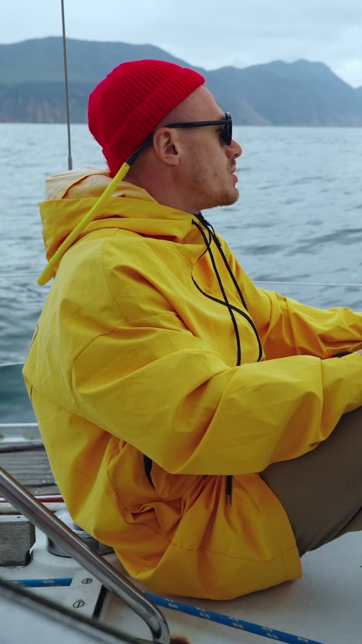 Mann im gelben Regenmantel und roter Mütze segelt auf dem Meer