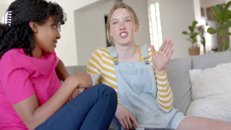 happy diverse teenage female friends talking and sitting on couch at home, slow motion