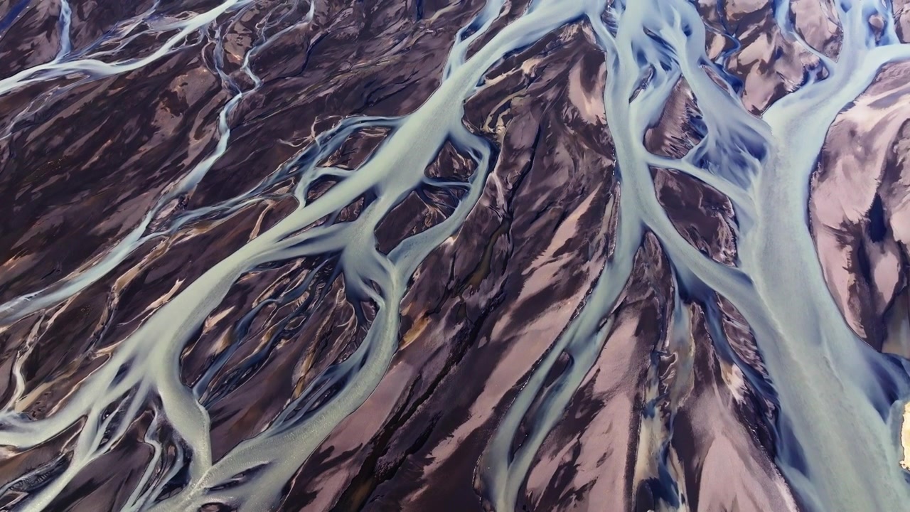 Aerial view of braided glacial rivers winding through dark volcanic landscape in Iceland