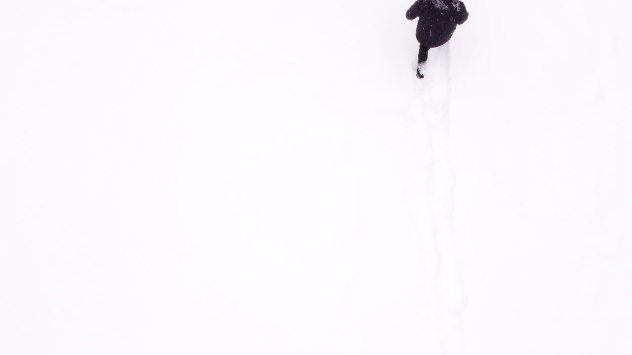 Aerial view of man walking in snow while holding a remote controller