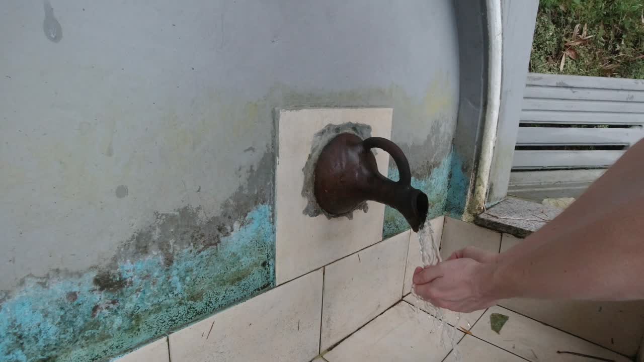 agua de manantial que viene de la pared de una jarra como el grifo, el hombre blanco toma un poco de agua para beber con las manos