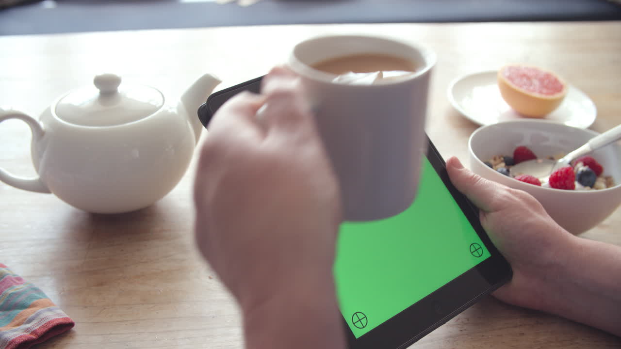 manos sosteniendo una tableta digital con pantalla verde en el desayuno