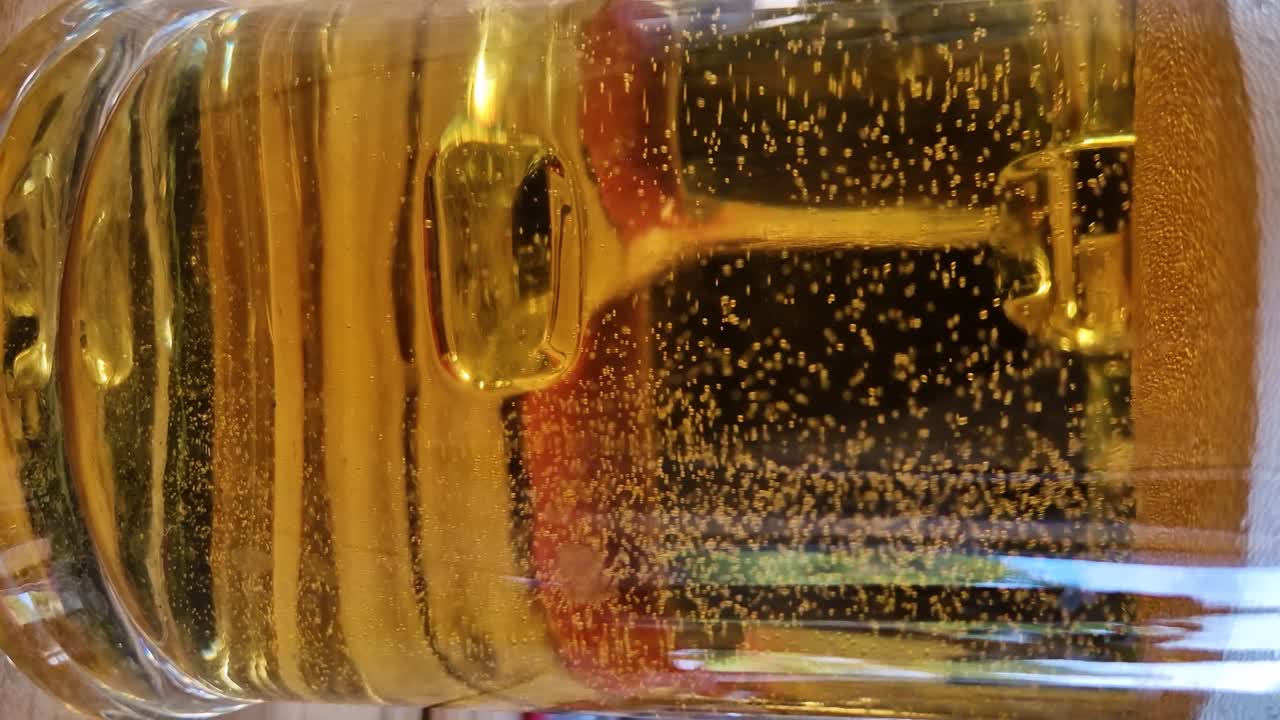 Bubbles of beer rises in transparent glass, close up vertical view