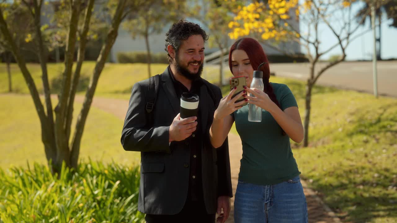 Man and Woman Walking Outdoors and Looking at Smartphone