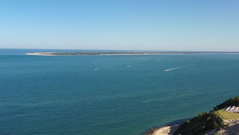 motorboats headed to dune du pilat in arcachon bassin france from cap ferret seen in the background, aerial flyover shot